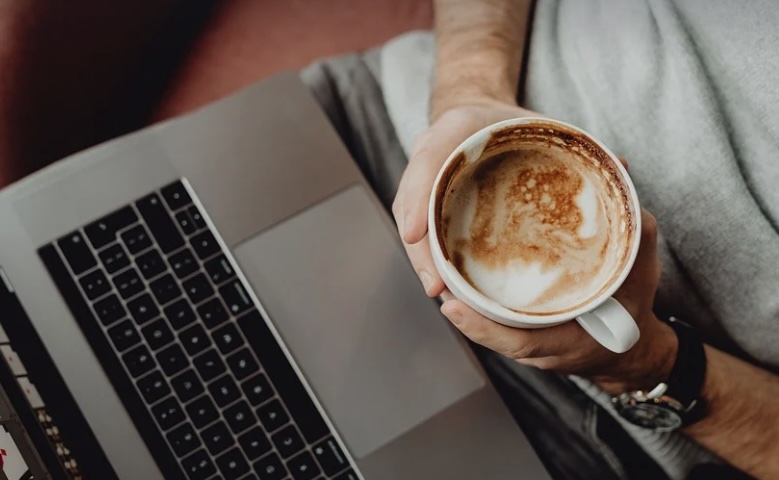 cup of coffee over held over laptop